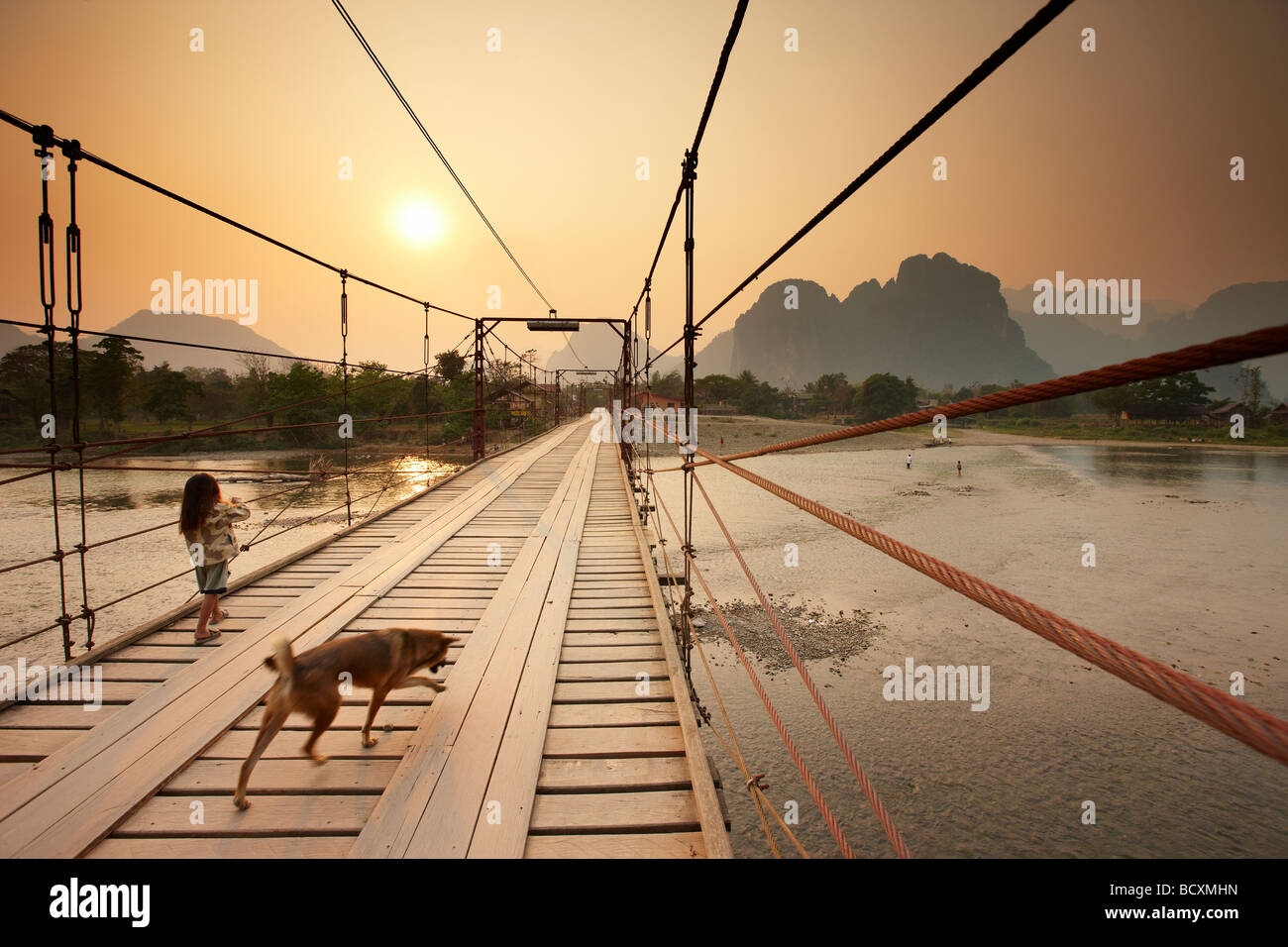 a girl and a dog crossing the bridge over the Nam Song River at Vang Vieng, Laos Stock Photo