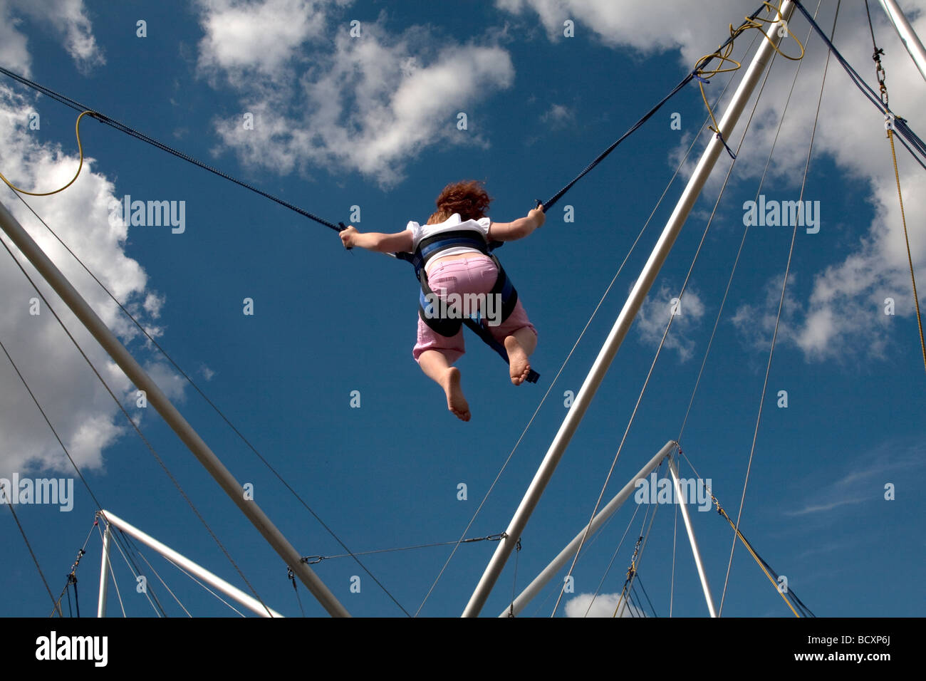 A young red haired girl enjoys a trampoline ride under blue skies at the 5th Colchester Military Festival in Essex, England Stock Photo