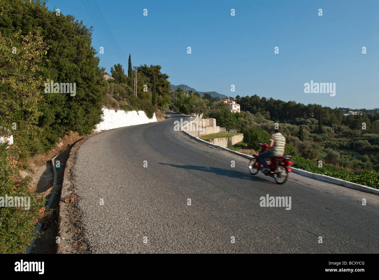 scenes from a greek aegean island. Driver on motorbike on a road leading up the hill to a village on a greek island. Stock Photo
