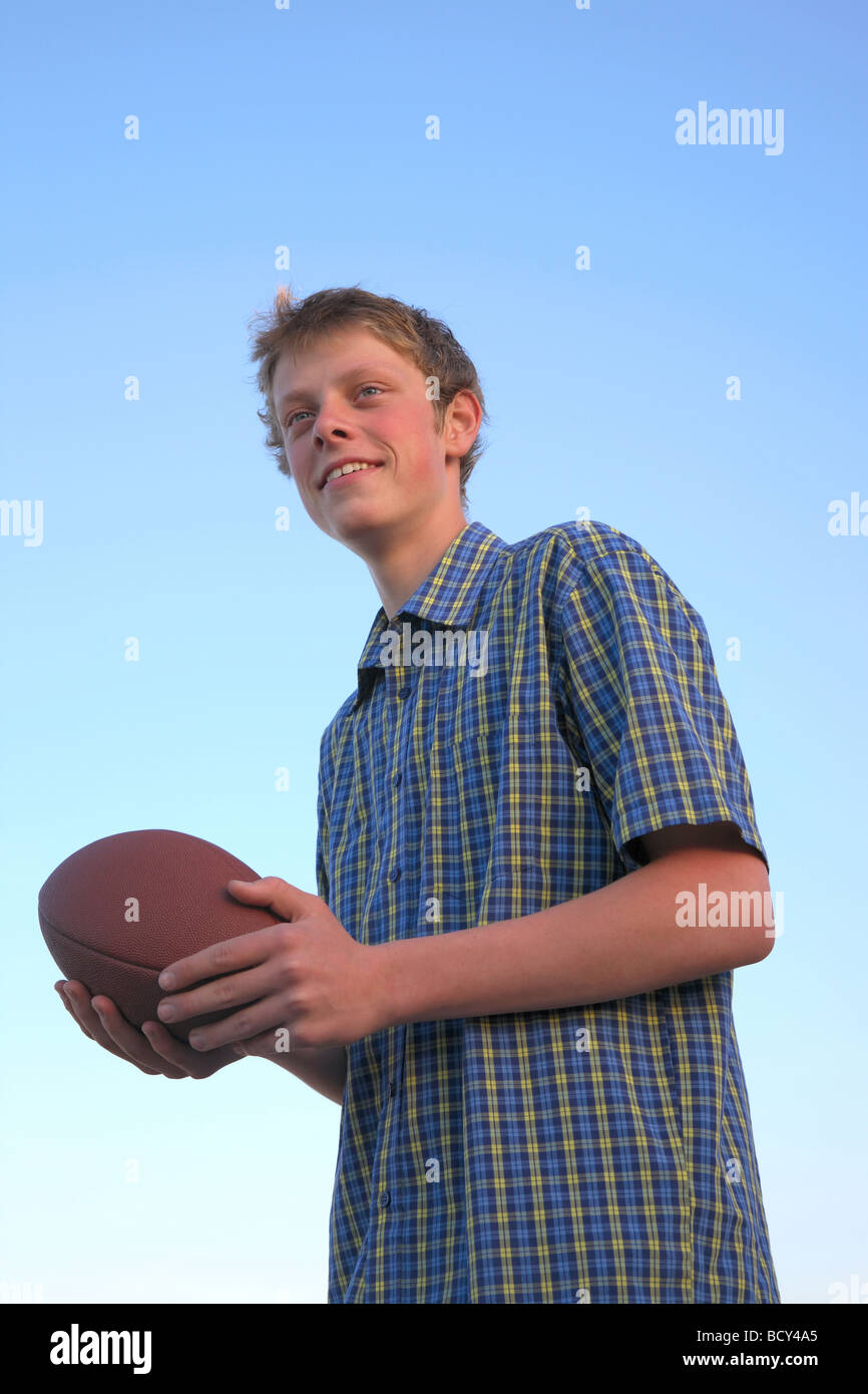 Teenage boy with an American football ready to throw against a blue sky in the sunset. Stock Photo