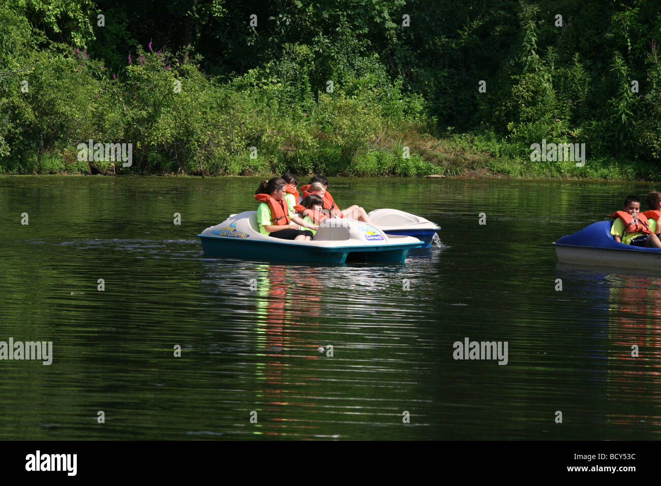 Children at a summer camp in paddle boats with life vests on a pond at the park. Stock Photo