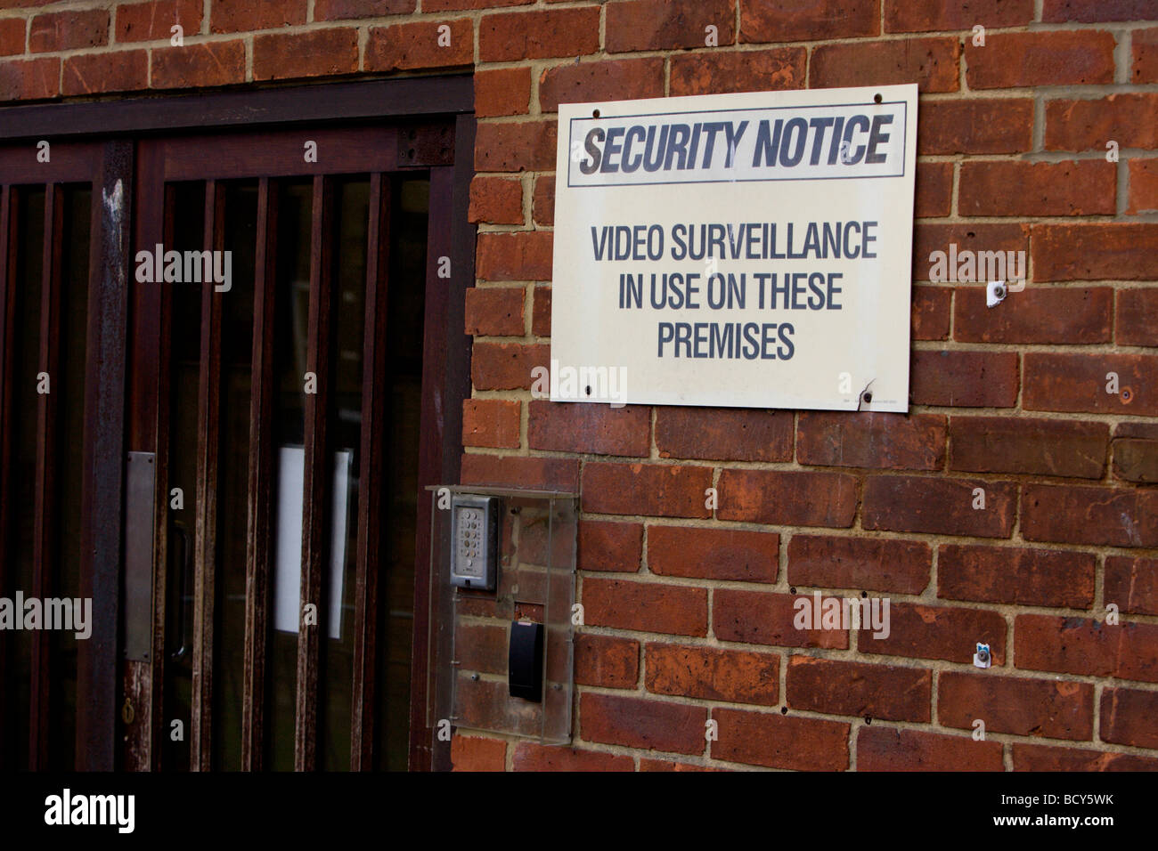Brown wooden office security door with a yelloe sign warning of video surveillance, Brighton, East Sussex. Stock Photo