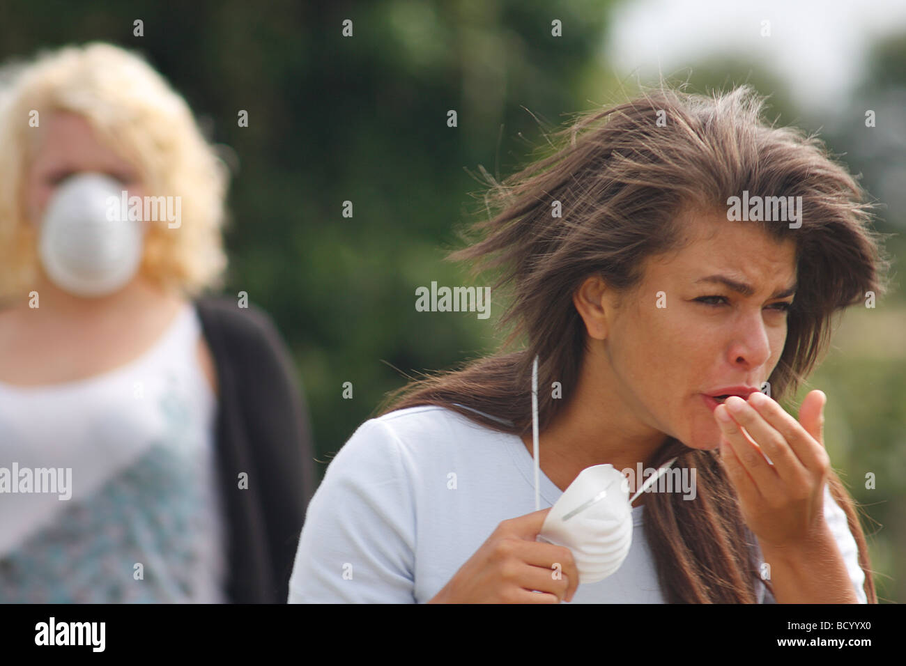 two women in street wearing filter masks one sneezing Stock Photo