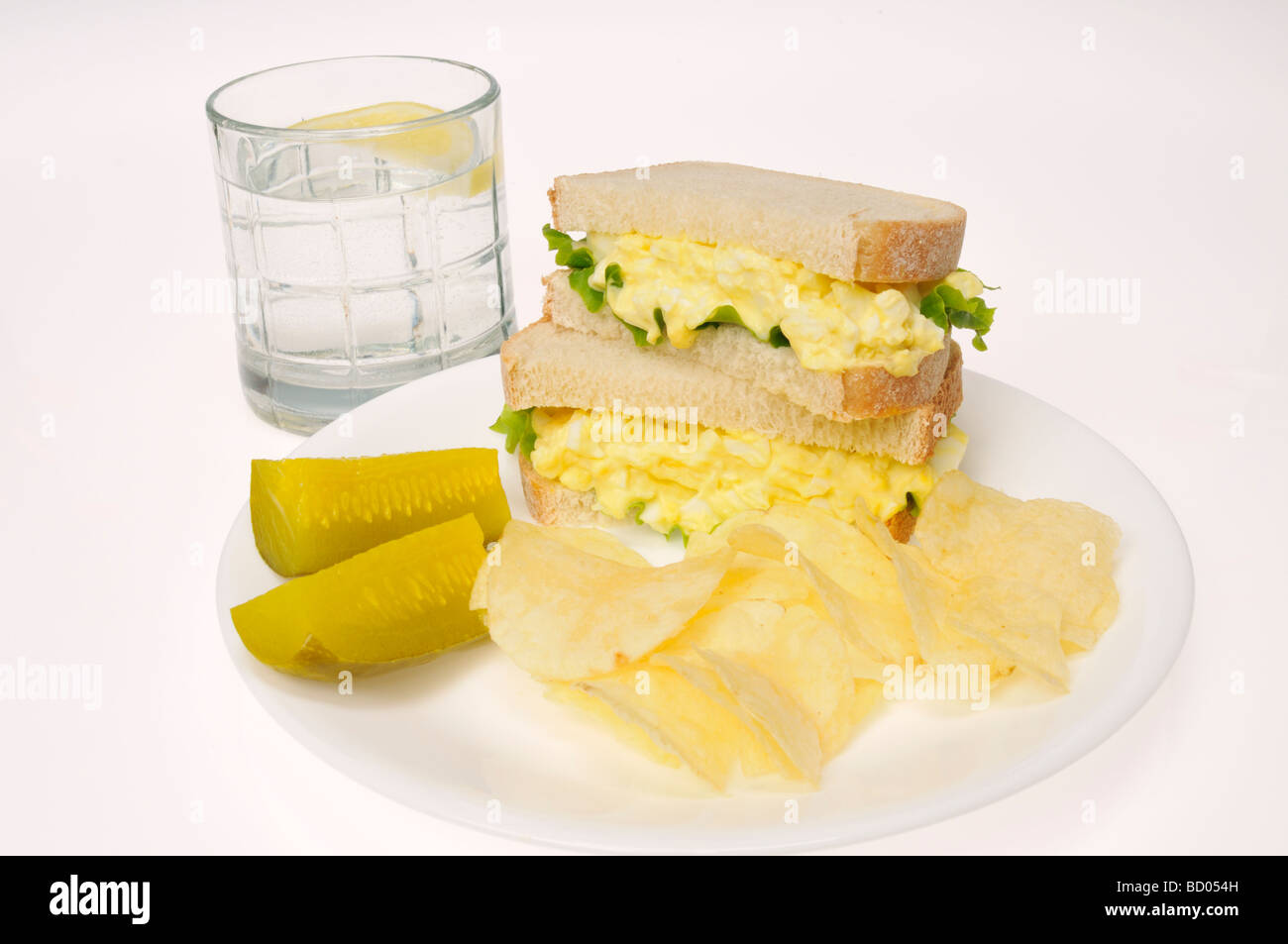 Egg mayo sandwich with potato chips and pickle on white plate with