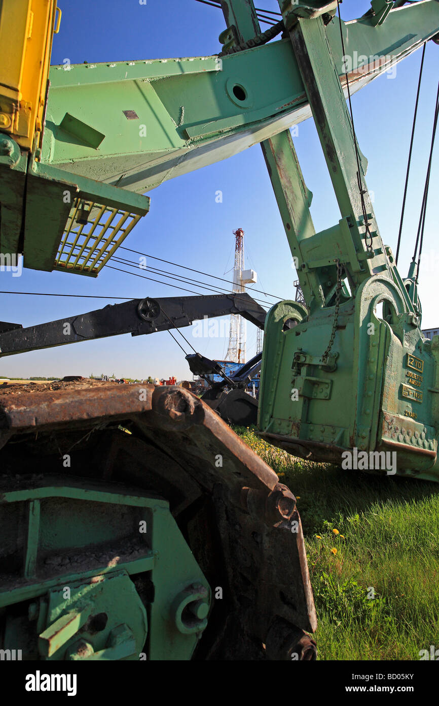 Old bucket loader at rest in field with oil drill derrick in background Stock Photo