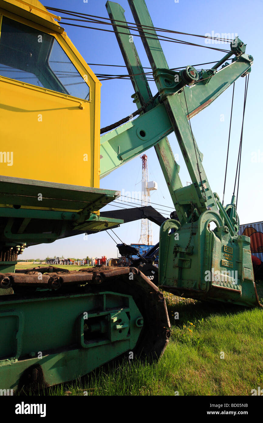 Old bucket loader at rest in field with oil drill derrick in background Stock Photo
