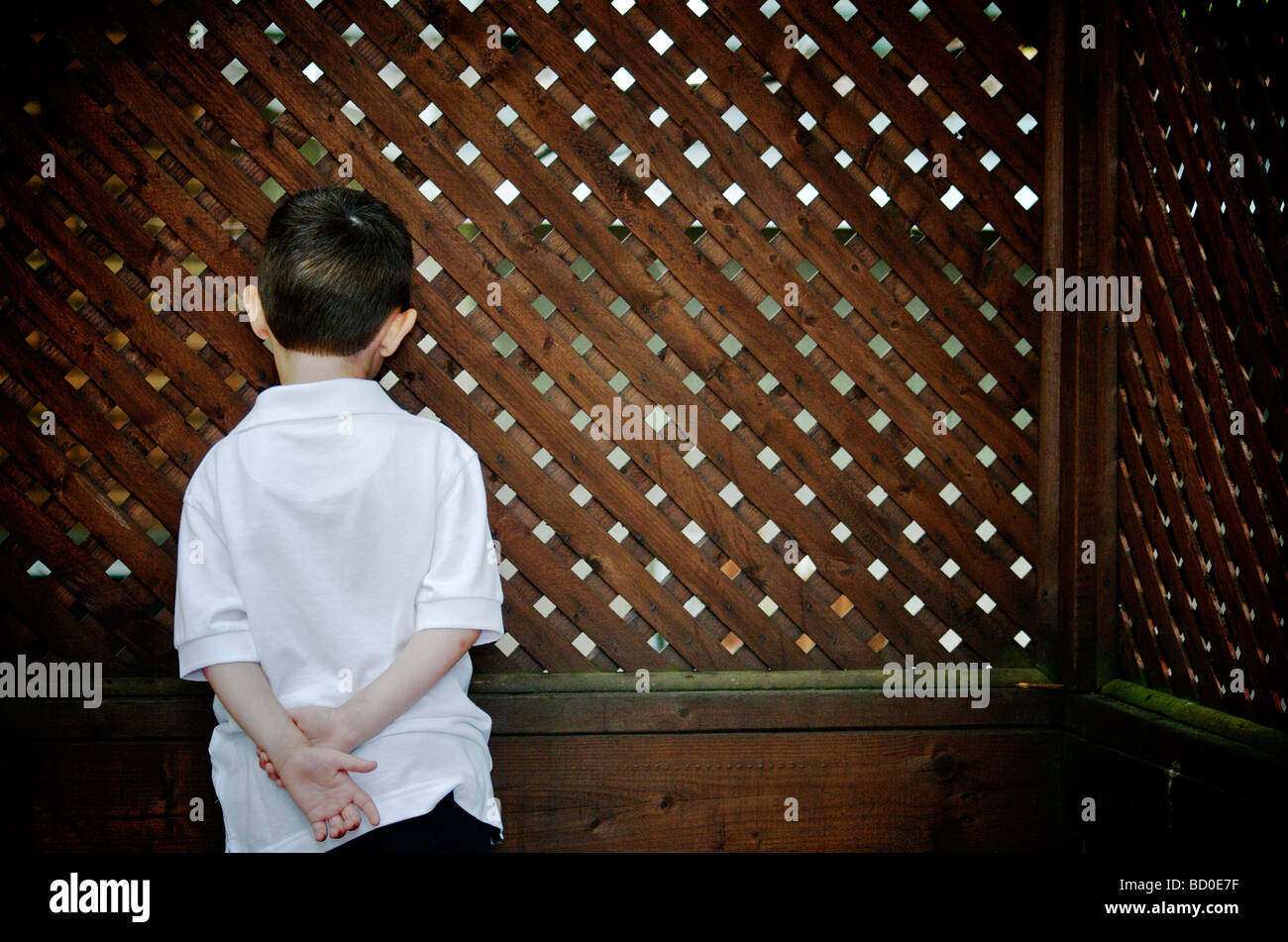 Back of a young boy looking through holes in a lattice wall, Otterburn park, Quebec Stock Photo