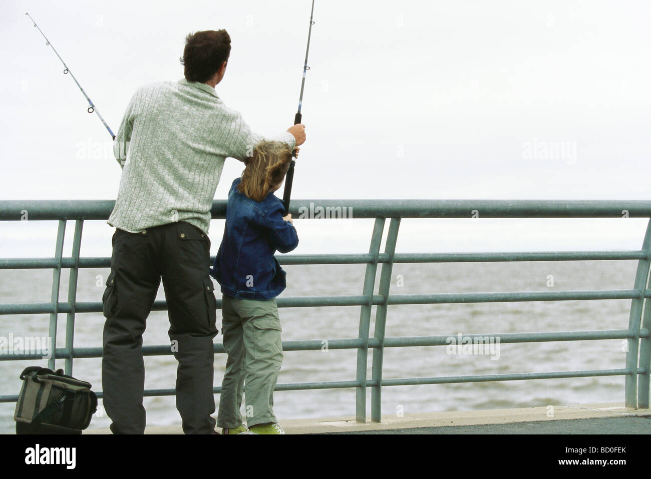 Father and son fishing from pier, father helping son with his