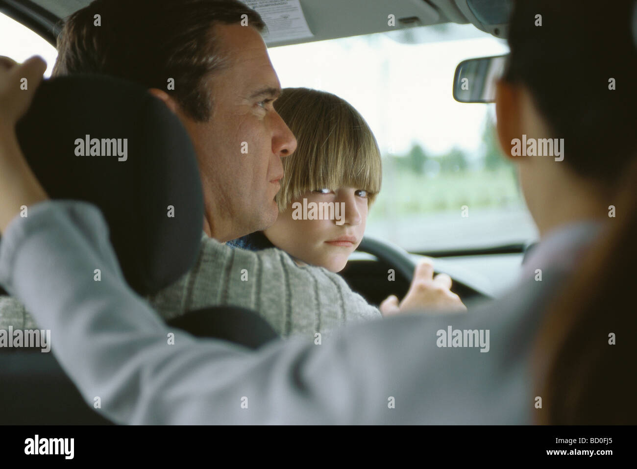 Boy sitting in father's lap in car, looking over shoulder at sister in back seat Stock Photo