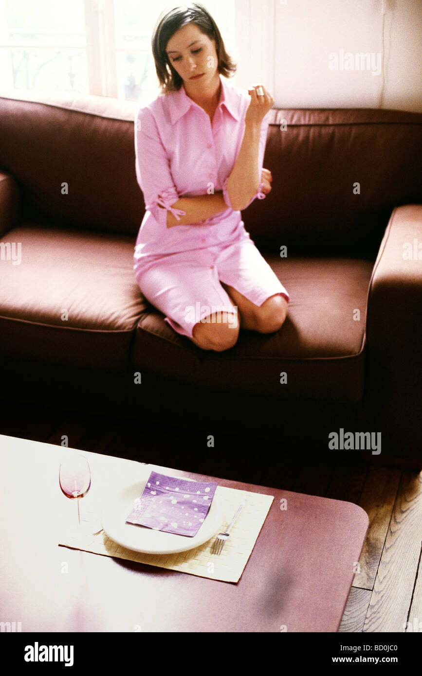 Woman sitting on sofa looking down a place setting set on coffee table, high angle view Stock Photo