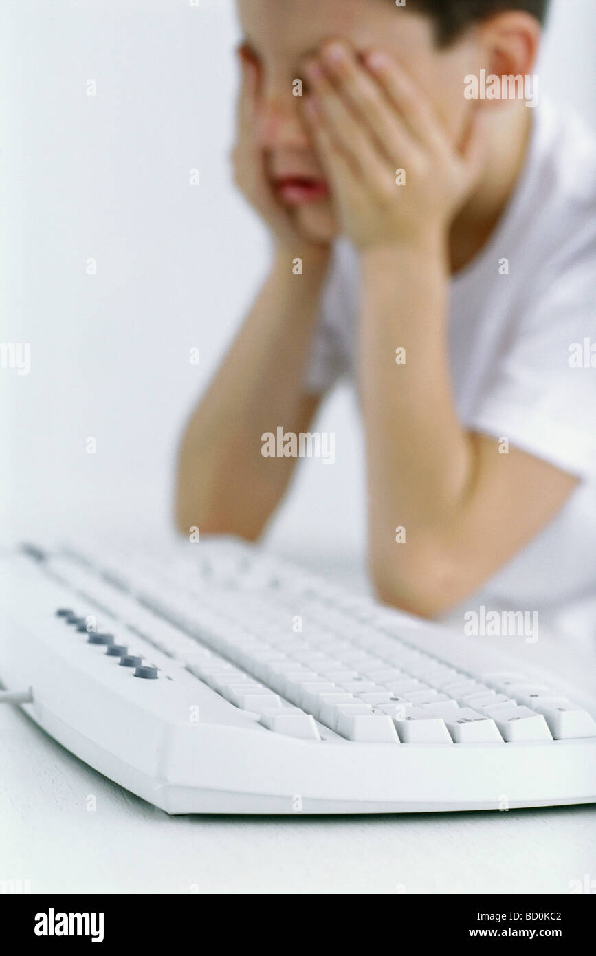 Boy holding head, computer keyboard in foreground Stock Photo
