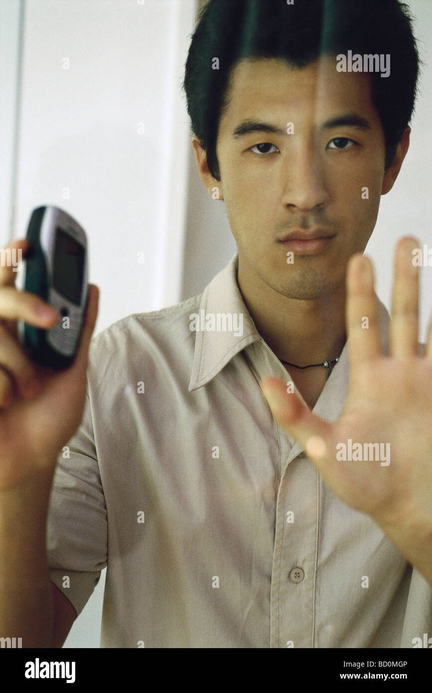 Man pressing hand against window, holding cell phone, looking at camera Stock Photo