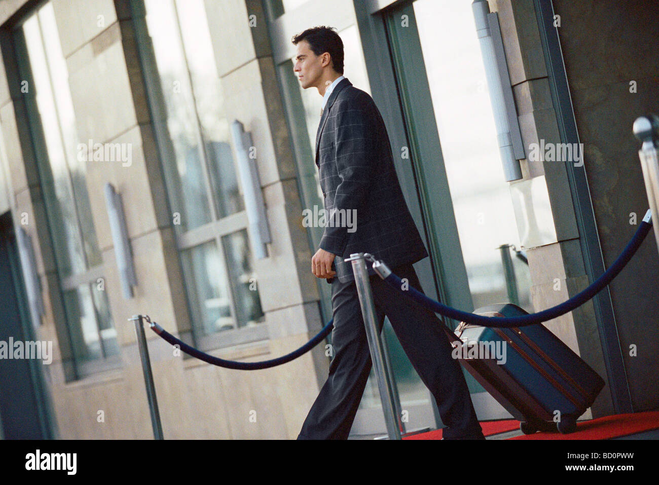 Businessman leaving hotel, pulling suitcase behind him Stock Photo