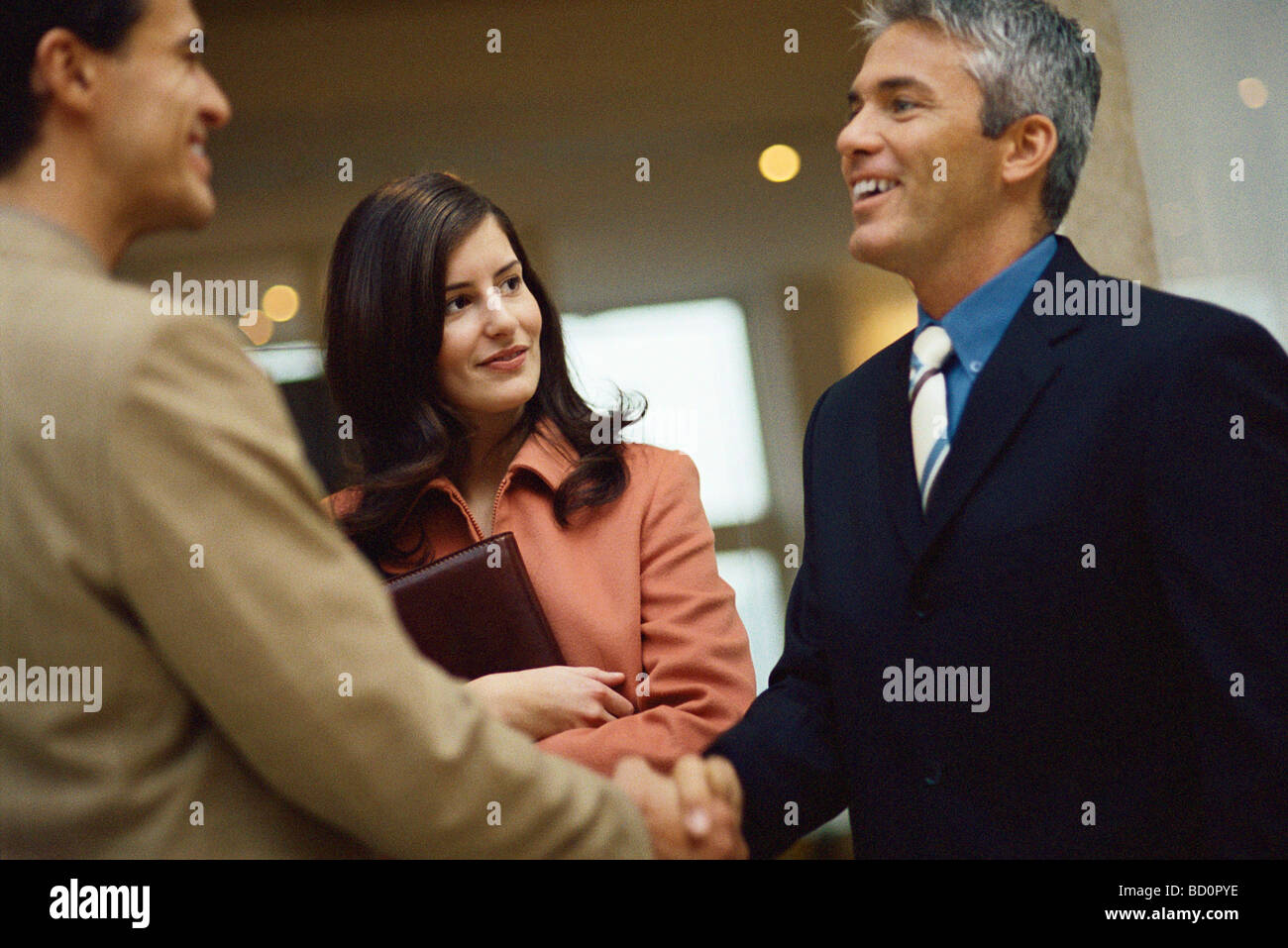 Businessmen shaking hands, female colleague standing nearby Stock Photo