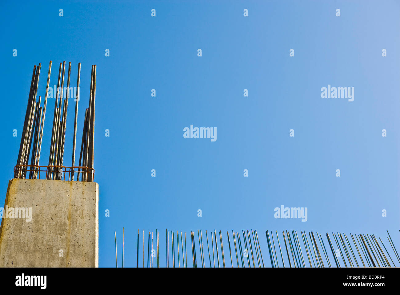 Exposed rebar protruding from unfinished concrete column against blue sky, low angle view Stock