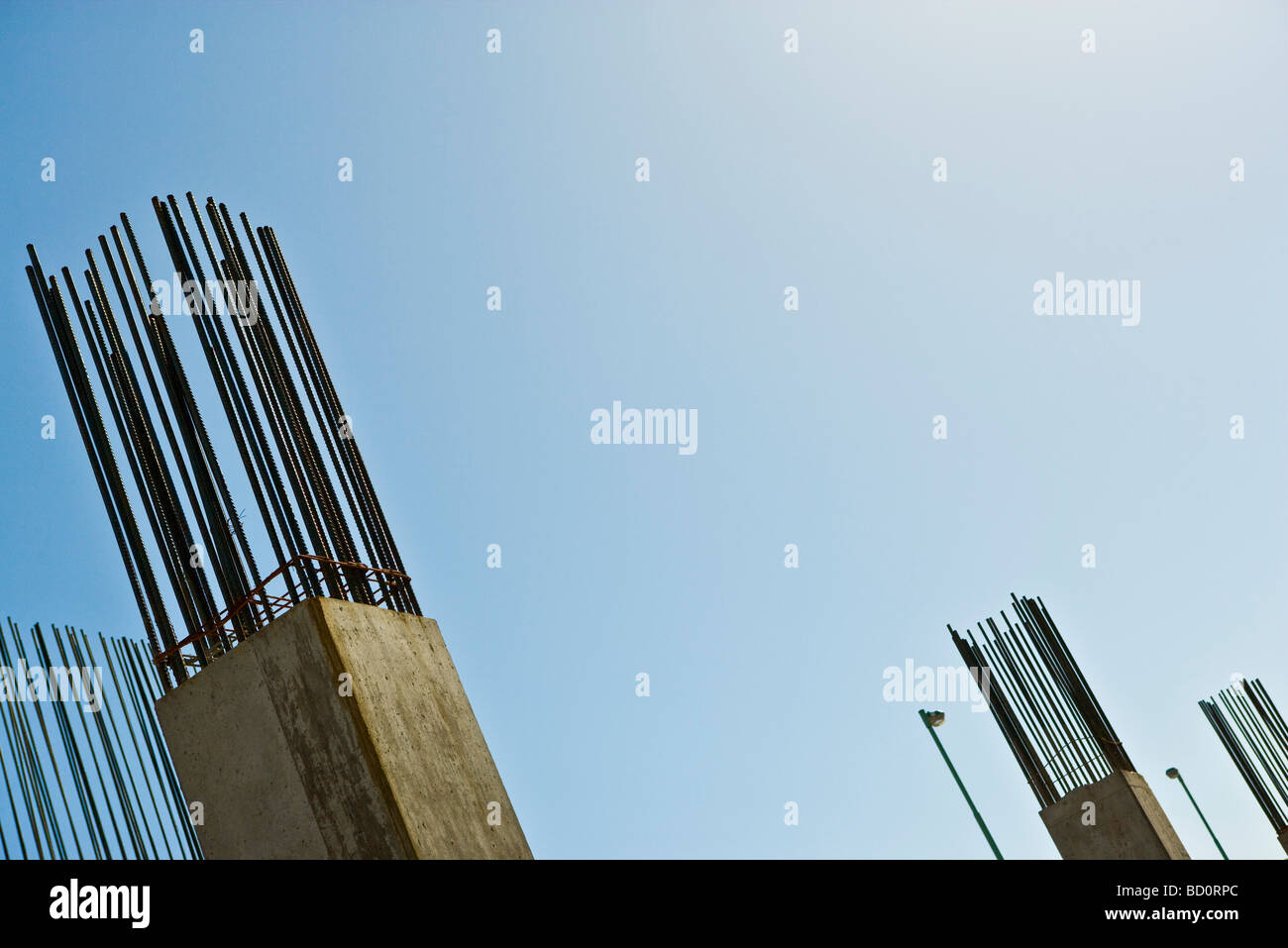 Exposed rebar protruding from unfinished concrete column against blue sky, low angle view Stock