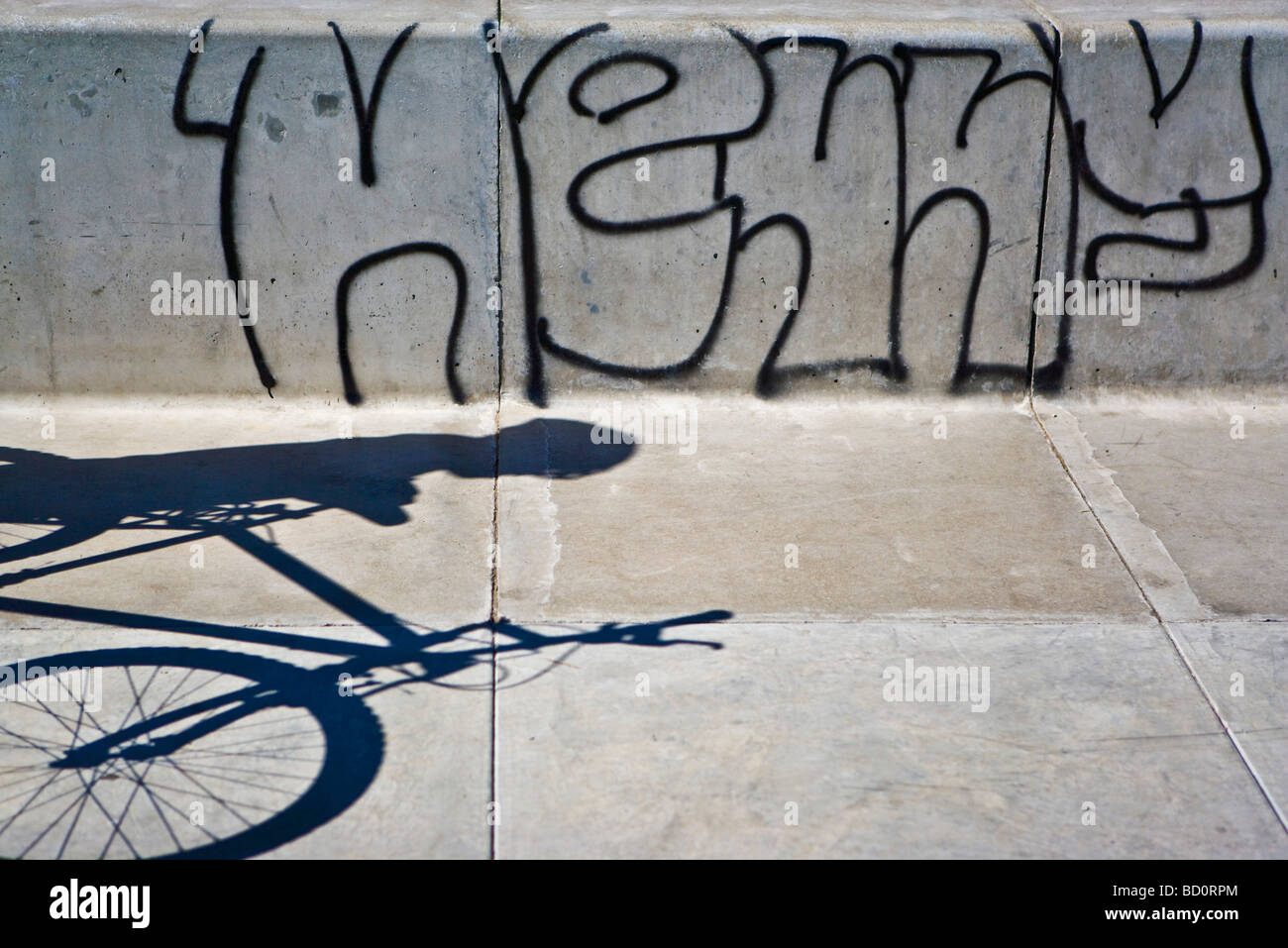 Shadow on sidewalk of person with bicycle, graffiti on wall Stock Photo