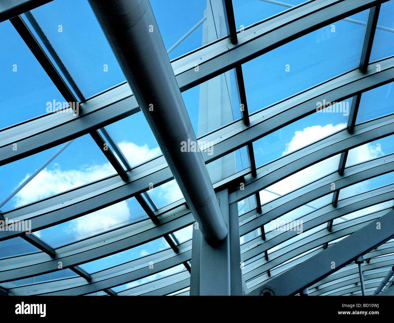 glass archway at airport looking upward to blue sky and white clouds architectural detail crossbeams and posts Stock Photo