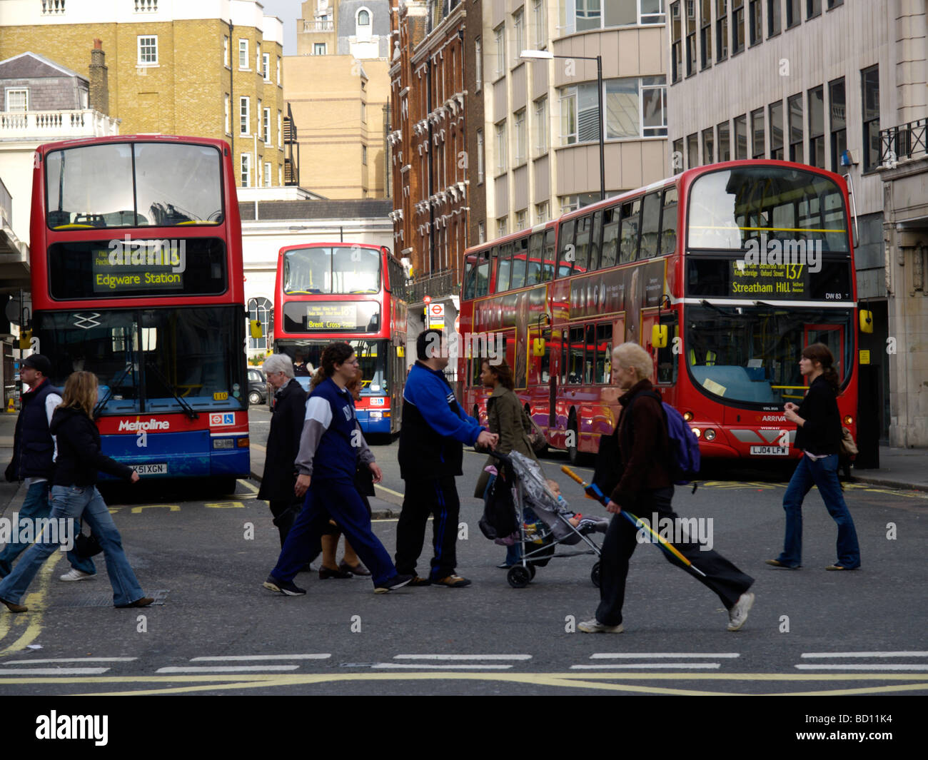People crossing the street with red London buses in the background image shot from Oxford Street London UK Stock Photo