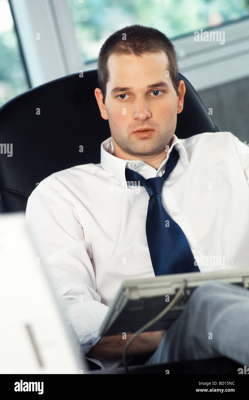 Man with feet up on office desk, typing on computer keyboard set on lap Stock Photo