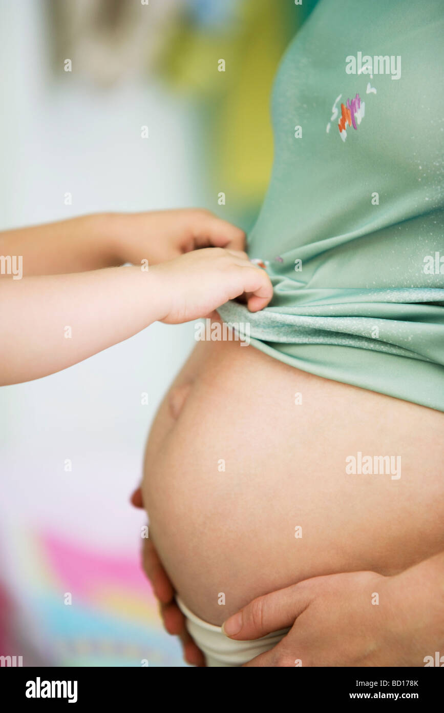 Child pulling mother's shirt down over pregnant belly Stock Photo Alamy