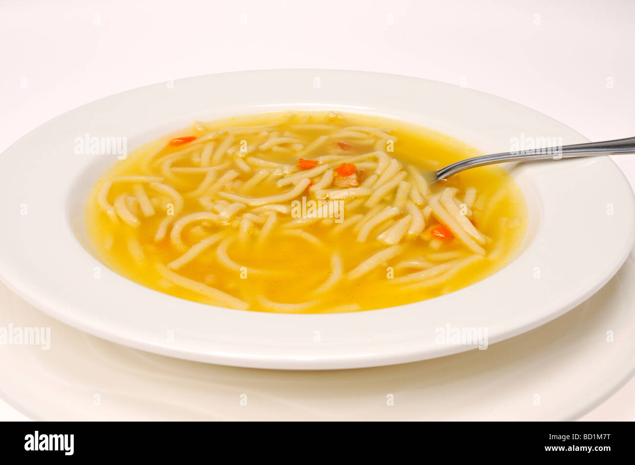 Bowl of chicken noodle soup with spoon on white background Stock Photo