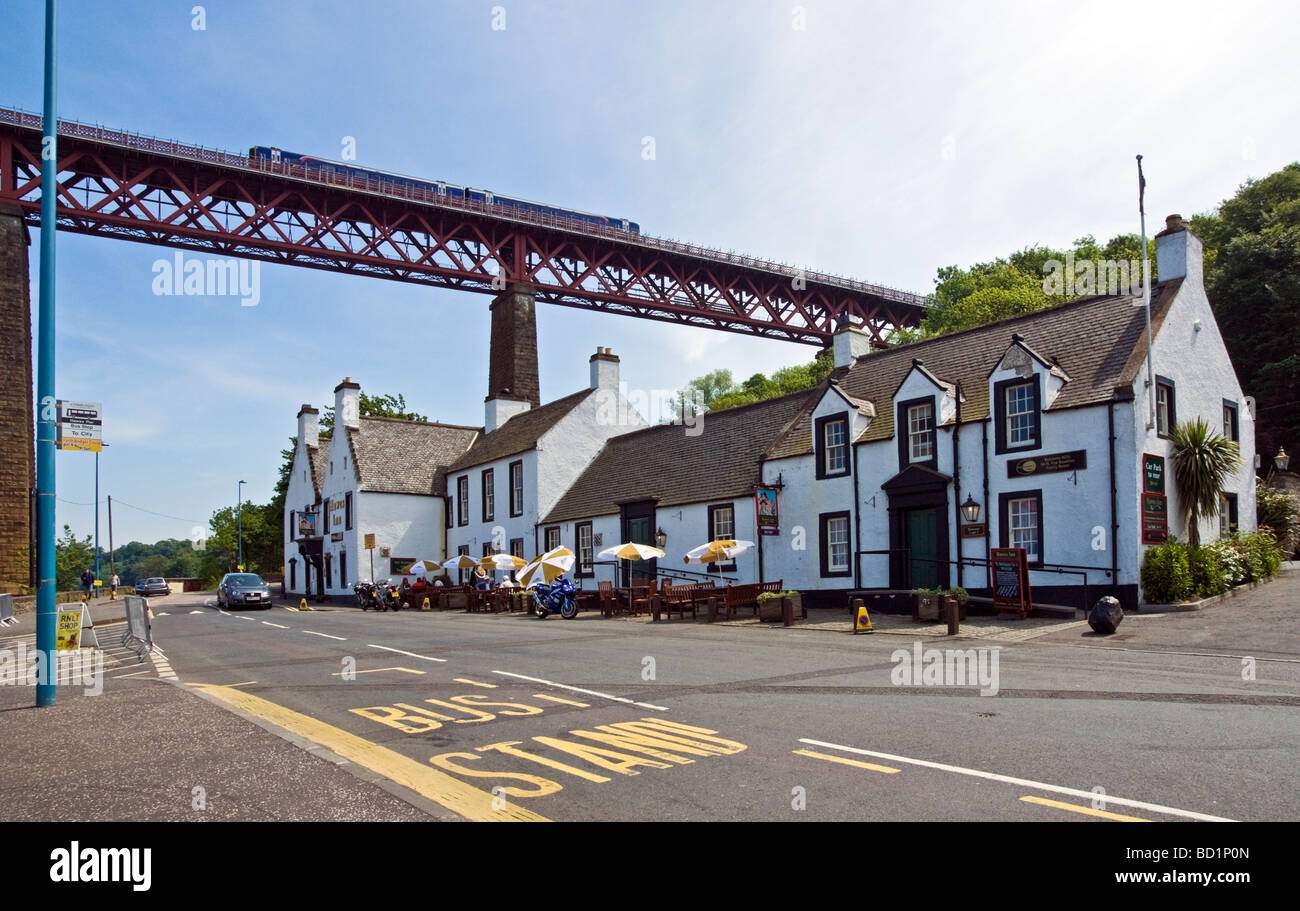 Famous Hawes Inn in South Queensferry Scotland with a First Scotrail DMU passes above on the Firth of Forth Rail Bridge Stock Photo
