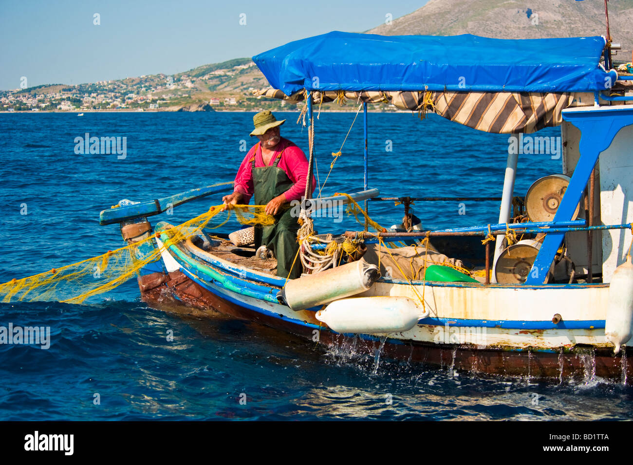 Greek fisherman pulling net in fishing boat in front of the coastline Stock Photo