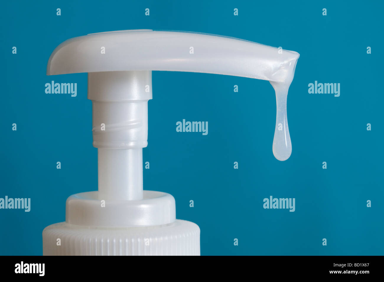 Close up of white antibacterial hand wash sanitizer plastic bottle pump dispenser with liquid soap dripping down against blue background Stock Photo