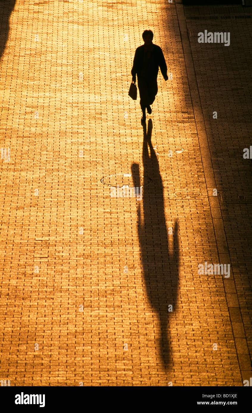 Woman pedestrian casts long shadow walking on sidewalk Odaiba district, Tokyo, Japan Stock Photo