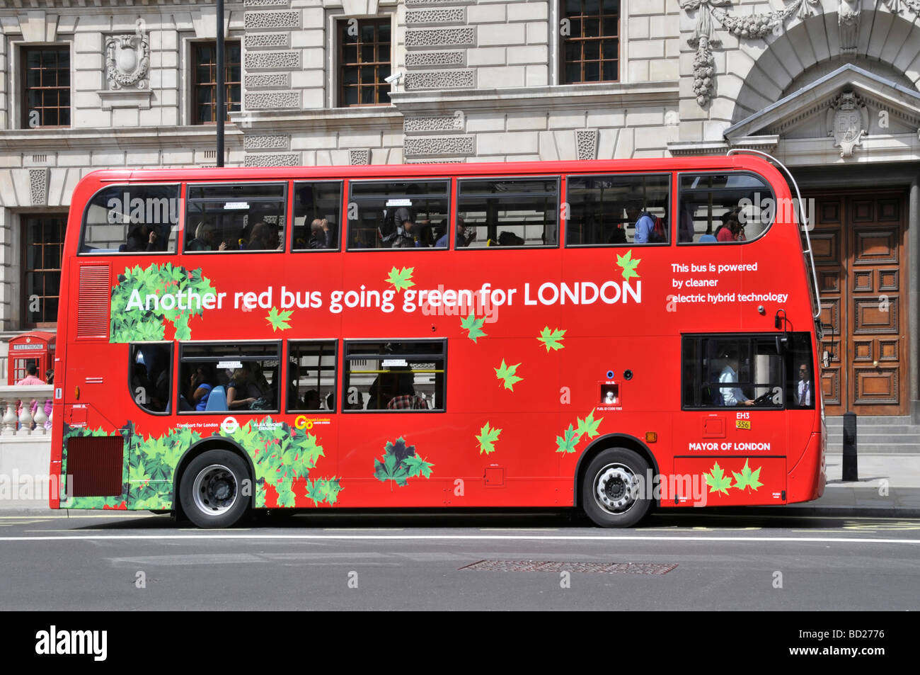 Side view of red double decker passenger bus going Green for public transport in London & powered by a cleaner electric hybrid technology England UK Stock Photo