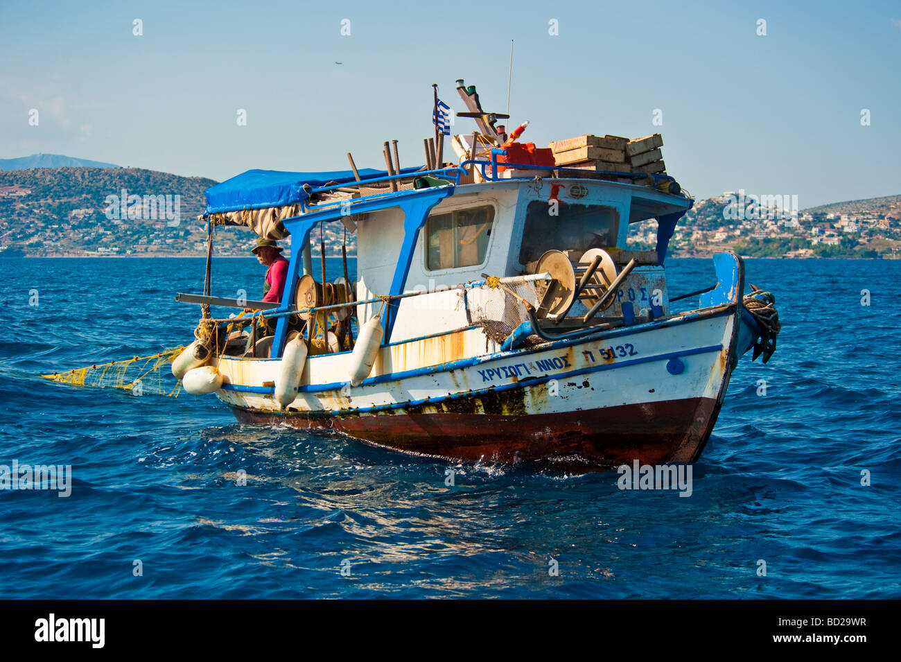 Greek fisherman pulling net in fishing boat in front of the coastline Stock Photo