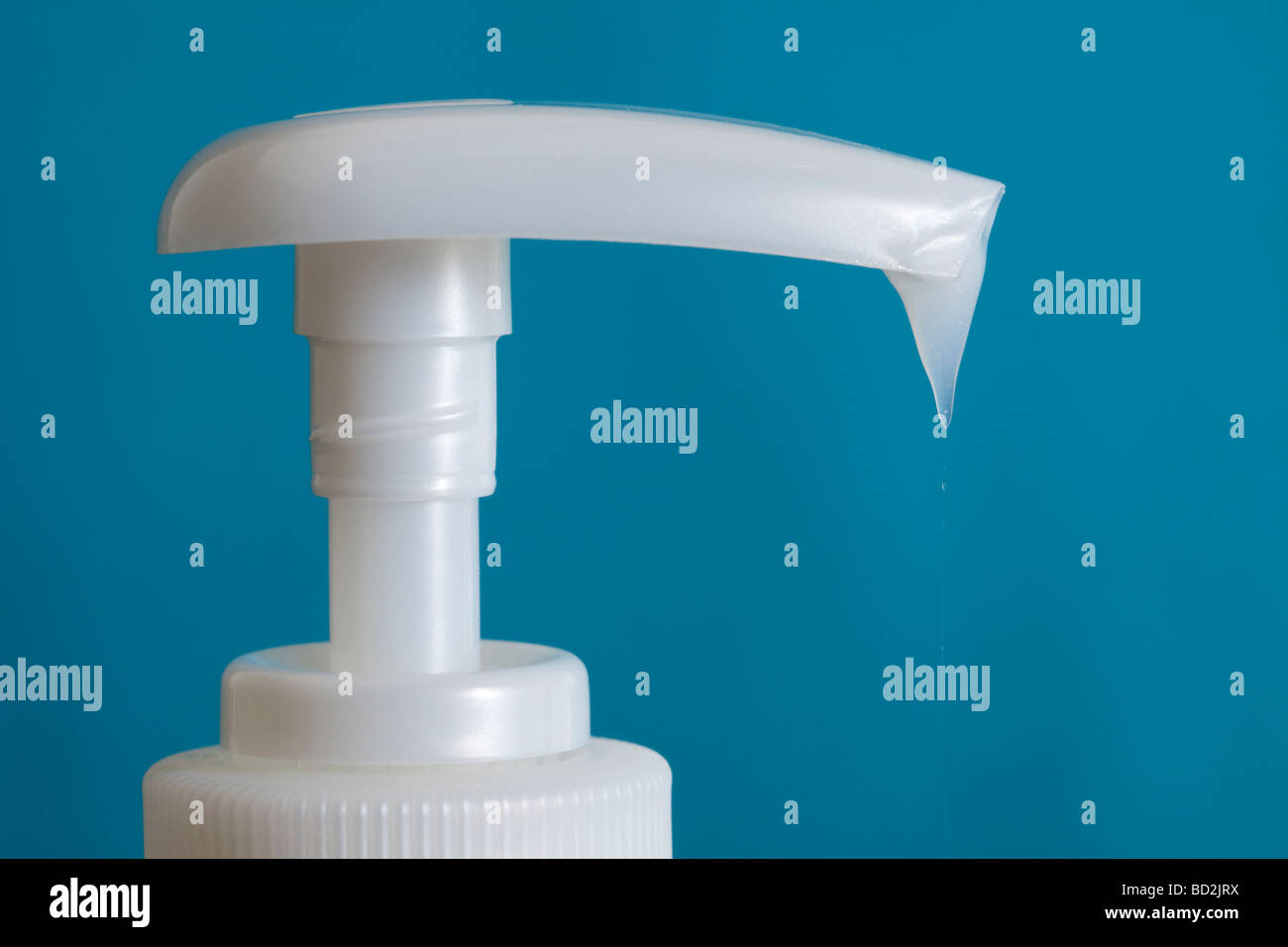 Close up of white antibacterial hand wash plastic bottle pump dispenser with soap dripping down against blue background Stock Photo