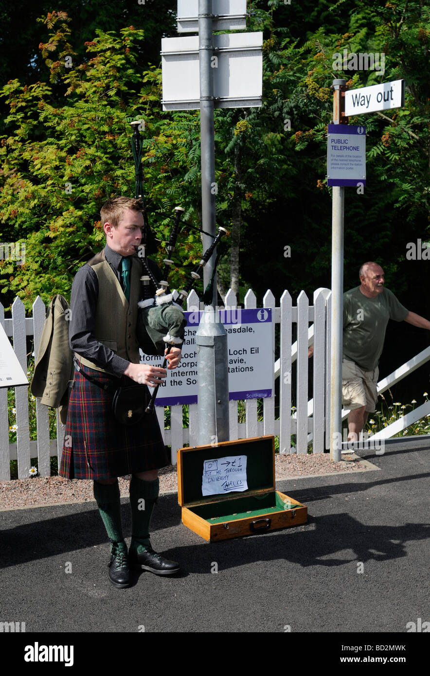 A lone piper stands on Glenfinnan Platform during the Jacobite Steam train Journey from Fort William to Mallaig in Scotland Stock Photo