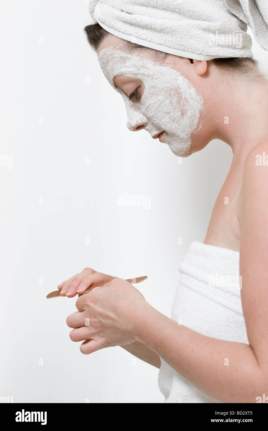 Woman filing her nails whilst wearing a towel and face mask Stock Photo