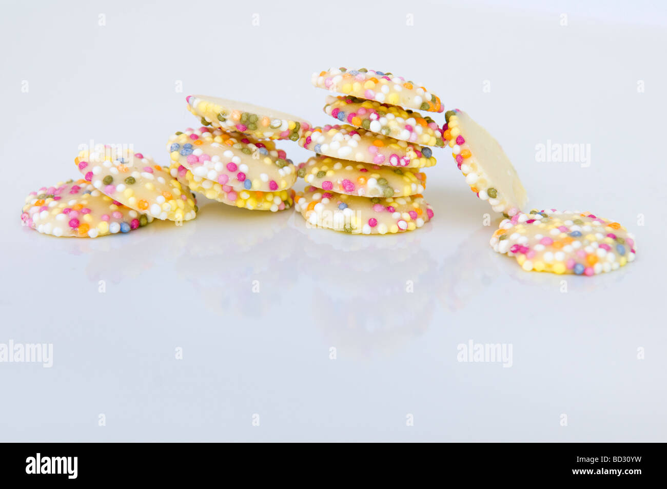 Still life shot of white chocolate button sweets covered in sprinkles taken against a white background with reflection Stock Photo