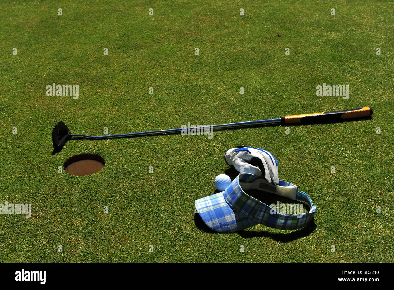 Golf course putting green with a putter, golf ball, ladies cloth sun visor and leather golfing glove Stock Photo
