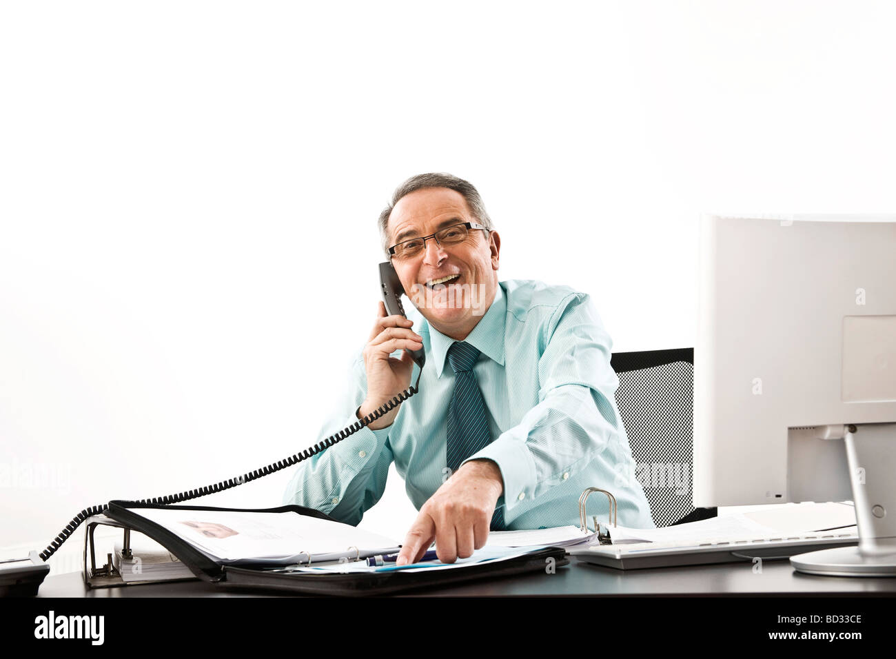 Manager with glasses sitting at his desk with a computer, speaking and laughing on the telephone Stock Photo