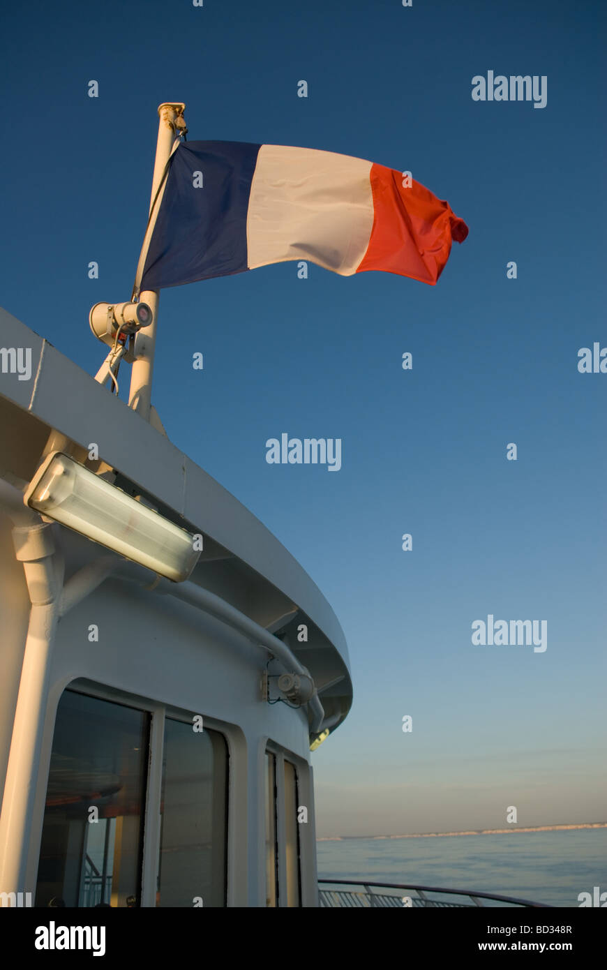 French flag tricolor blowing in the wind attached to cabin on a ship ferry with blue sunny sky at sunset Stock Photo