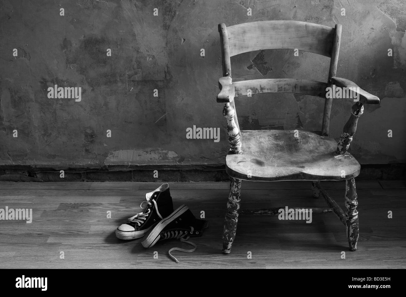 wooden chair on wooden floor, with bare plaster wall, shoes on floor Stock Photo