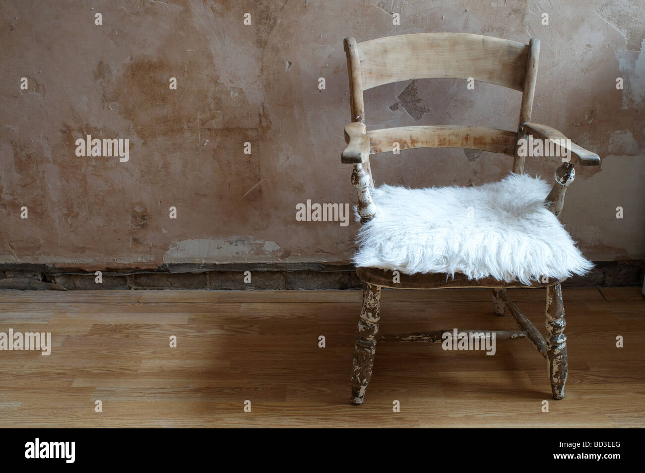 wooden chair on wooden floor, with bare plaster wall, fluffy white cushion Stock Photo