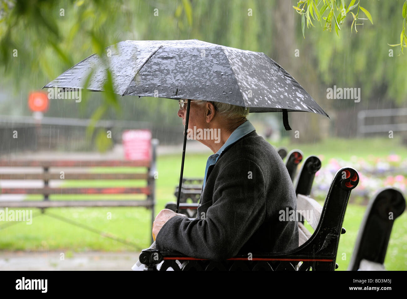 Elderly man sheltering from the rain with umbrella in Worcester England