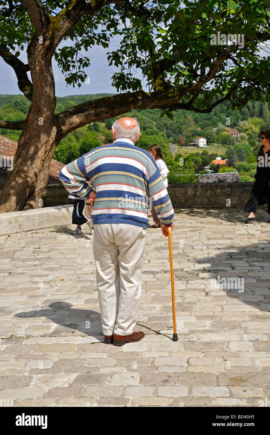 Elderly retired old man standing resting relaxing with walking stick on bright sunny day in France Stock Photo