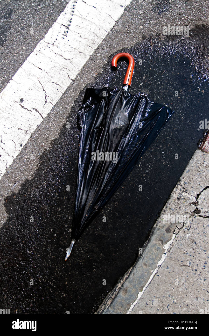 Black umbrella in plash on street. Sunny day. Stock Photo