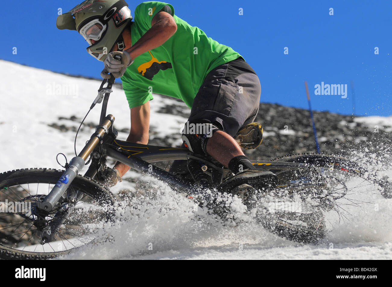 A downhill mountain biker corners at speed on summer snow on a glacier