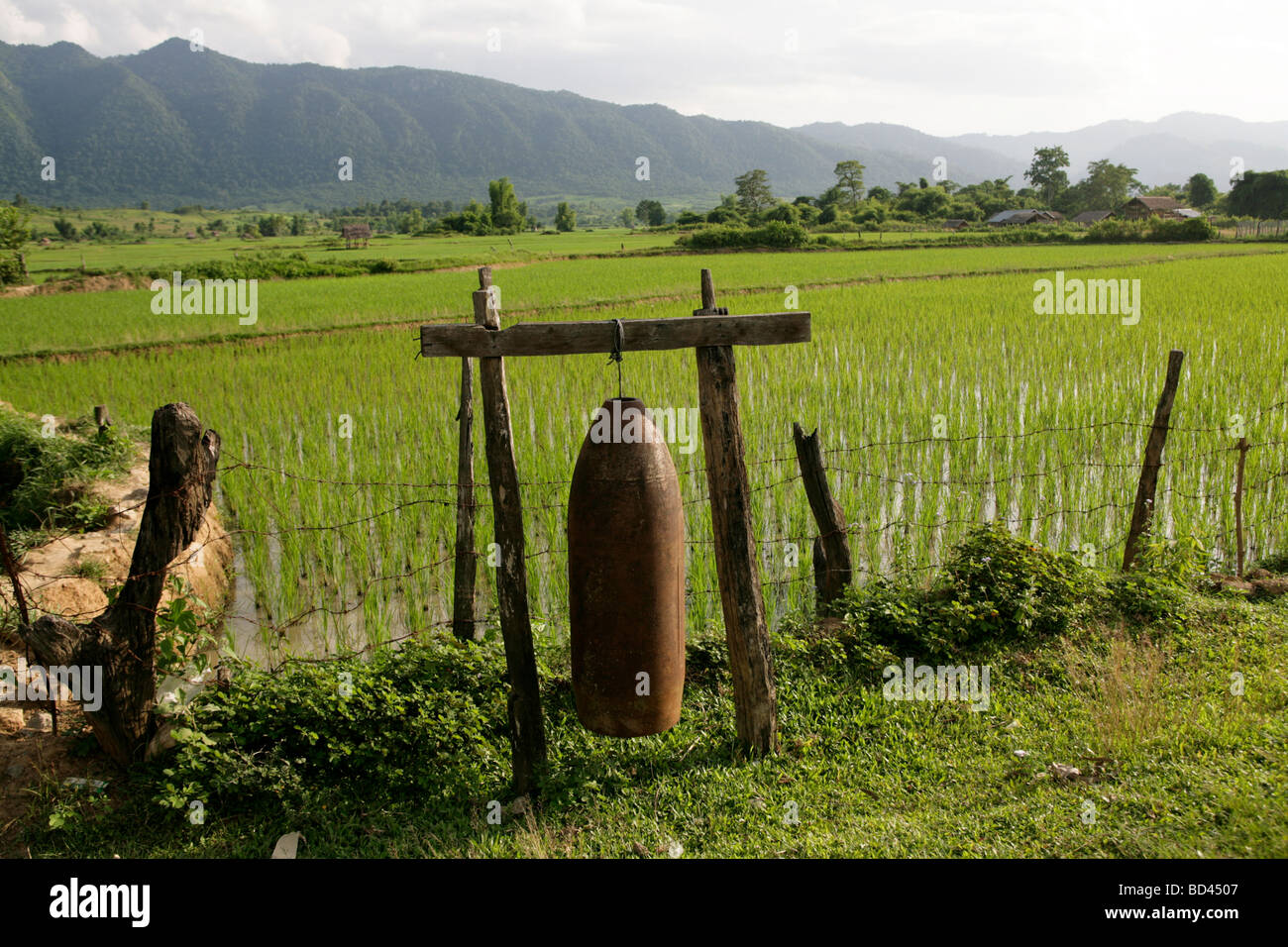 Xieng Khouang, Laos, 2006 : A  500 pound bomb casing dropped by the US in the Vietnam War is used as a gong beside rice paddies Stock Photo