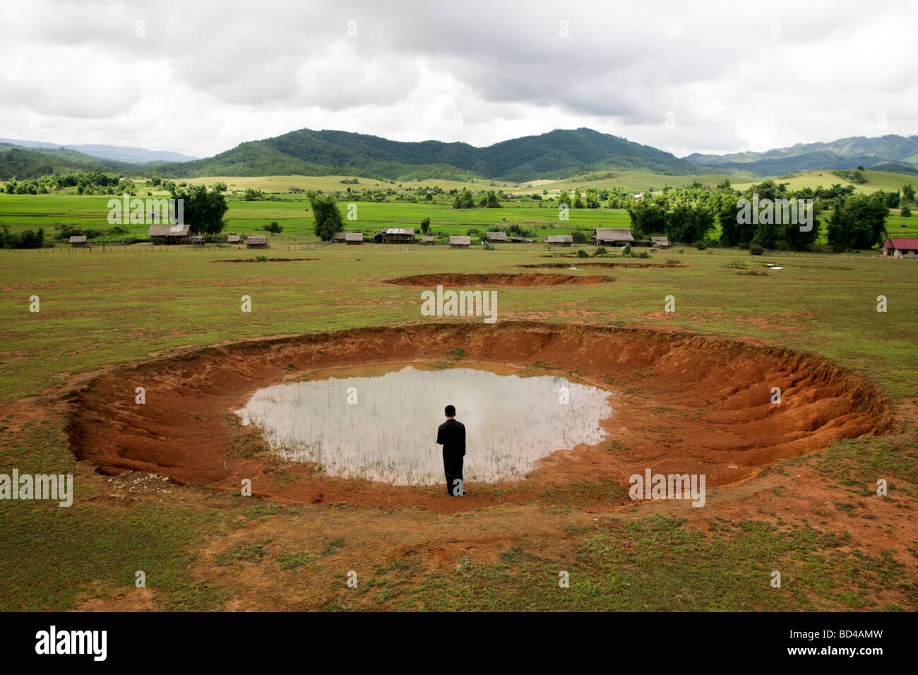 Xieng Khouang, Laos : A man stands beside a bomb crater,one of a row, made more than 30 years ago by US Airforce carpet bombing Stock Photo