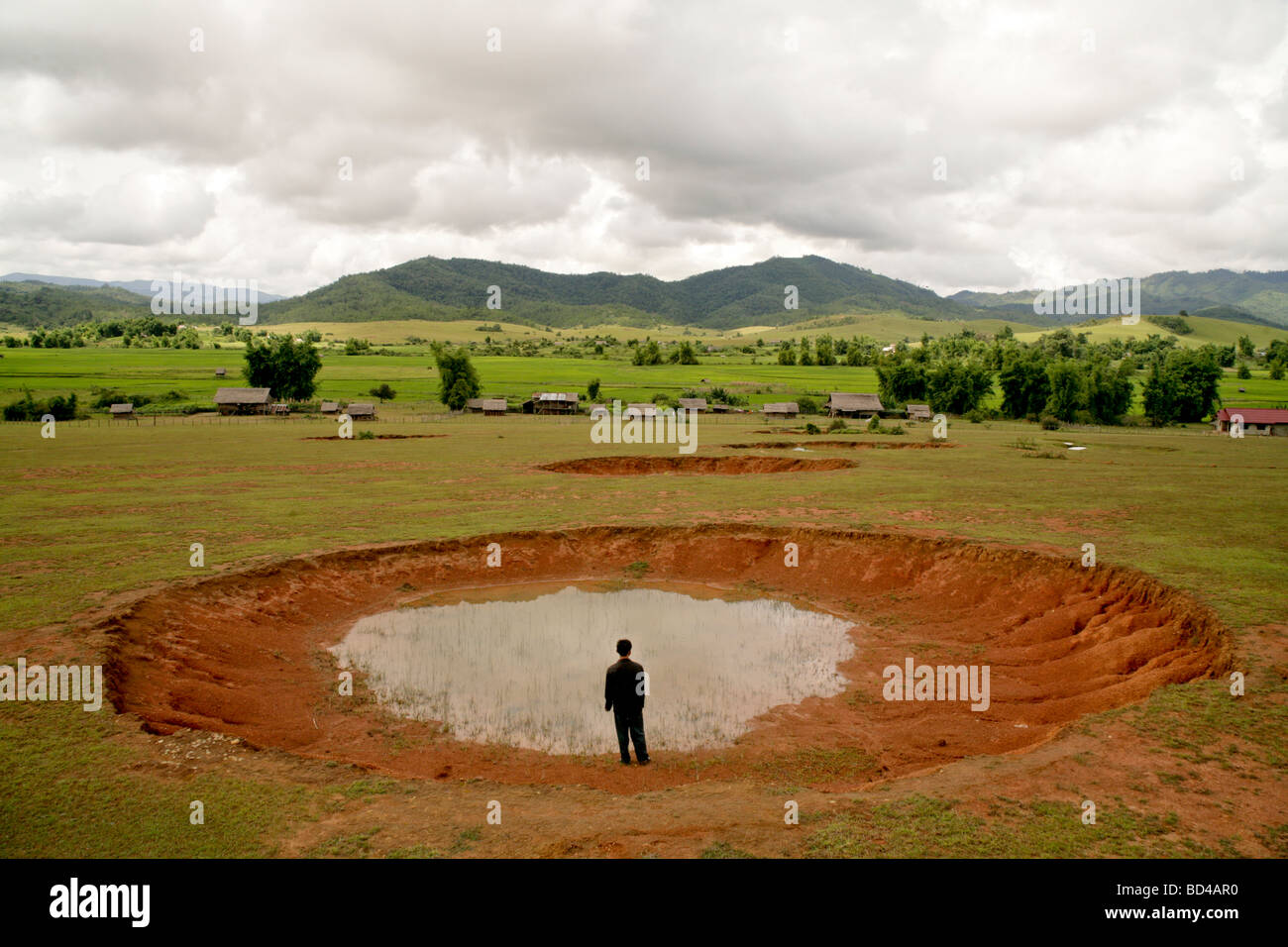 Xieng Khouang, Laos : A man stands beside a bomb crater,one of a row, made more than 30 years ago by US Airforce carpet bombing Stock Photo