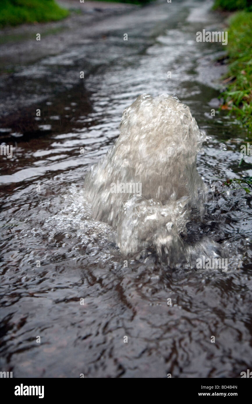 Water gushing out of drain and water running down country lane after heavy rainfall. Stock Photo