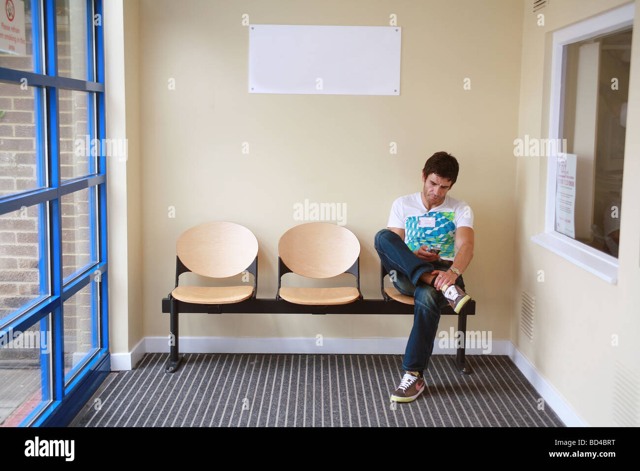 white adult male in a waiting room sending texts on his mobile phone Stock Photo